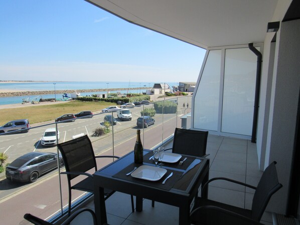 A balcony with a table set for two, overlooking a parking lot and a beach.