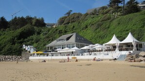 Ein Hotel direkt am Strand mit einem großen Gebäude, Außenbereich und einer Hügelkulisse.