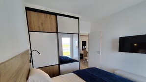Ein Schlafzimmer mit einem Bett, einem an der Wand montierten Fernseher und Blick durch eine offene Tür.