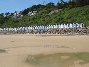 A beach with a row of beach huts and houses on a hillside.
