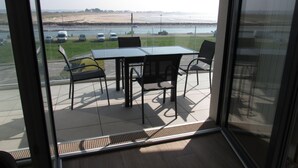 Ein Balkon mit Tisch und Stühlen, Blick auf einen Strand und geparkte Autos.