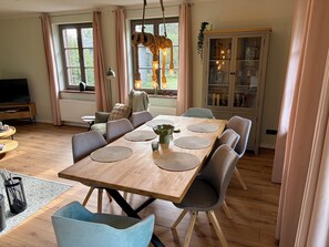 A dining area with a wooden table, grey chairs, and a hanging light fixture. - Family vacation home with a sauna and a fireplace (Kamminke)