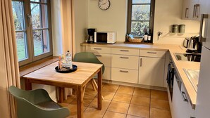 Cozinha compacta com mesa de jantar, cadeiras, relógio, micro-ondas e janela com vista para árvores.