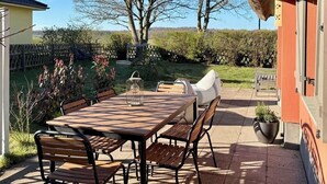 Um pátio externo com mesa e cadeiras, um teto de palha e vista para árvores e uma cerca.