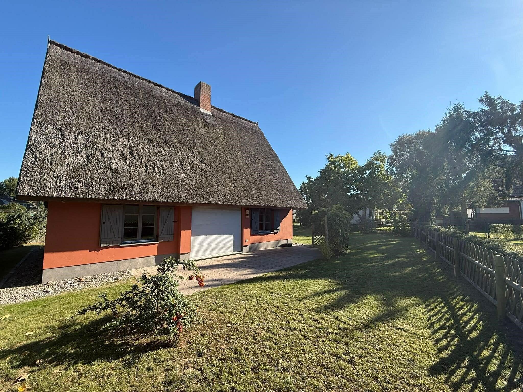Et traditionelt hus med stråtækt tag, en lille veranda og en velplejet græsplæne.