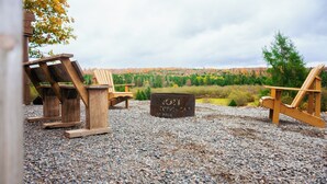 Tunnelmallinen ulkotila, jossa on maalaishenkinen istuinalue, Adirondack-tyyliset tuolit ja metallinen nuotiopaikka.