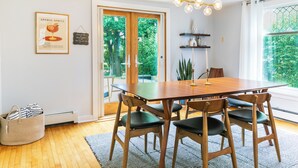 Un comedor con mesa y sillas de madera, una lámpara colgante y vistas a través de un ventanal.