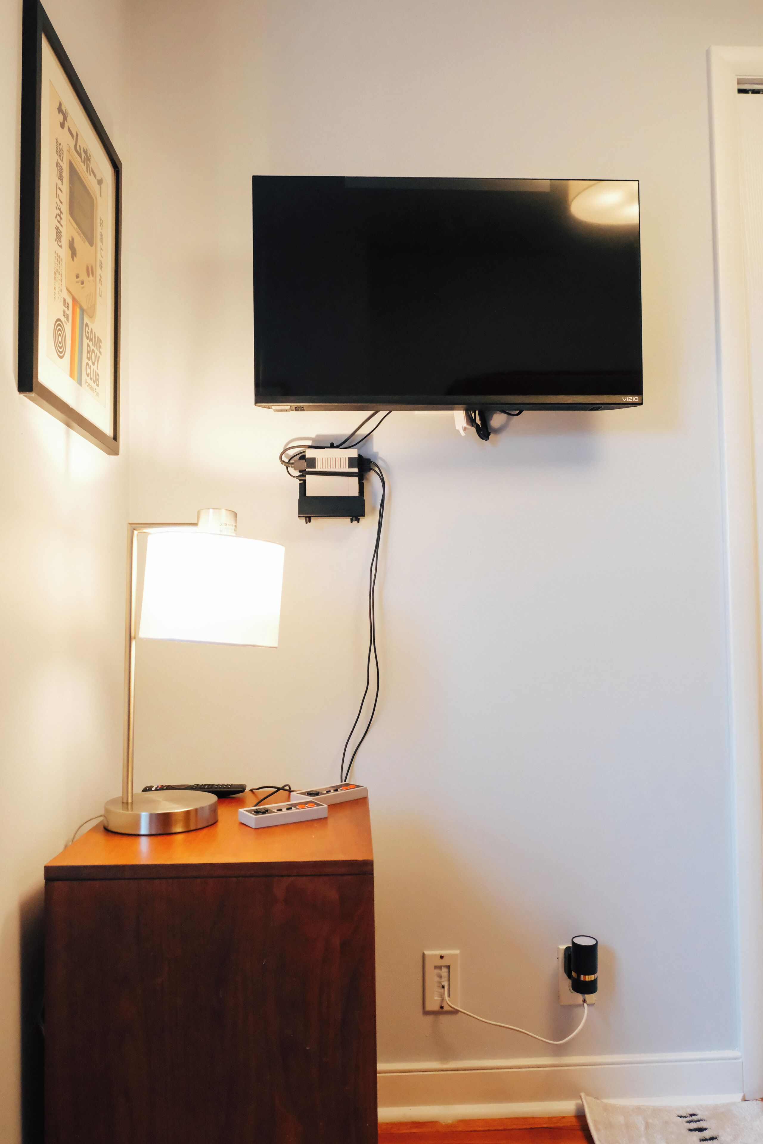 A flat-screen TV mounted on a wall, a desk with a lamp, and a power strip.