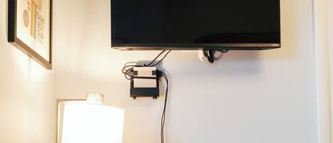 A flat-screen TV mounted on a wall, a desk with a lamp, and a power strip.