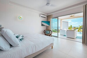 A bedroom with a bed, a chair, and a view of a pool and buildings. - New Sea-View Villa w/ Private Pool & Jacuzzi – SXM - Villa Maé (St Martin)
