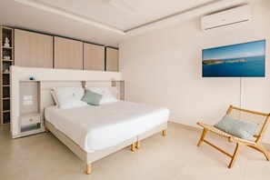 A bedroom with a bed, a chair, a TV, and a wardrobe. - New Sea-View Villa w/ Private Pool & Jacuzzi – SXM - Villa Maé (St Martin)