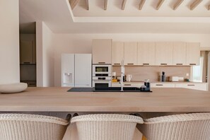 A modern kitchen with a central island, built-in appliances, and light wood cabinetry. - New Sea-View Villa w/ Private Pool & Jacuzzi – SXM - Villa Maé (St Martin)