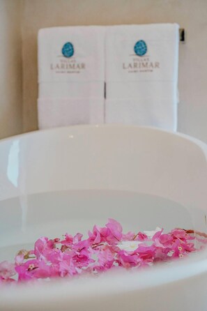Eine Badewanne mit rosa Blütenblättern, die im Wasser treiben, und im Hintergrund zwei Handtücher an einem Handtuchhalter.