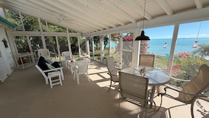 Uma área de estar coberta ao ar livre, com mesa e cadeiras, com vista para o mar.