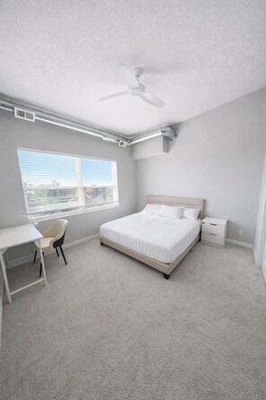 Un dormitorio con cama, escritorio, silla, mesita de noche y ventilador de techo.