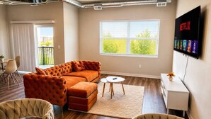 A modern living room with a sofa, chairs, a TV, and a window. - Family-Friendly 2BR with Amenities, WiFi & Parking (Des Moines)