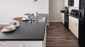 A modern kitchen with a central island, pendant lighting, and a black refrigerator. - Family-Friendly 2BR with Amenities, WiFi & Parking (Des Moines)