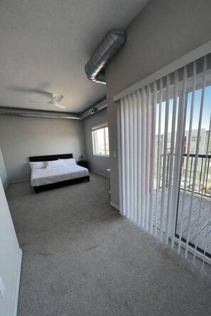 Une chambre à coucher avec un lit, un ventilateur de plafond, un radiateur et une grande fenêtre avec des stores.
