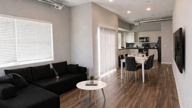 Un salon moderne avec un canapé noir, une table basse ronde et un coin repas comprenant une table et des chaises blanches.