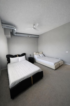 Une chambre avec deux lits, un ventilateur de plafond et des conduits apparents.
