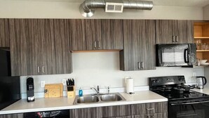 A modern kitchen with a built-in dishwasher, a stove, and a microwave. - Elegant 2BR Apartment with Fast WiFi & Free Parking (Des Moines)