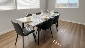 A dining area with a table set for four, black chairs, and large windows with blinds. - Elegant 2BR Apartment with Fast WiFi & Free Parking (Des Moines)
