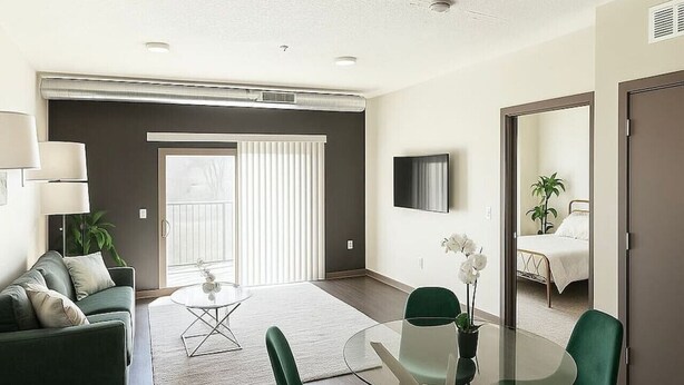 Un salon moderne avec un canapé vert, une table basse en verre et des fauteuils verts. Une porte-fenêtre coulissante donne accès à un balcon.