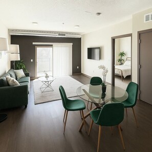 A modern living room with a green sofa, a glass coffee table, and green chairs. There is a sliding glass door leading to a balcony. - Chic Des Moines 1BR with Amenities & Prime Location (Des Moines)