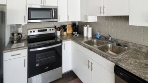 Une cuisine moderne avec des armoires blanches, un four à micro-ondes en acier inoxydable, une cuisinière et un évier à deux bacs.