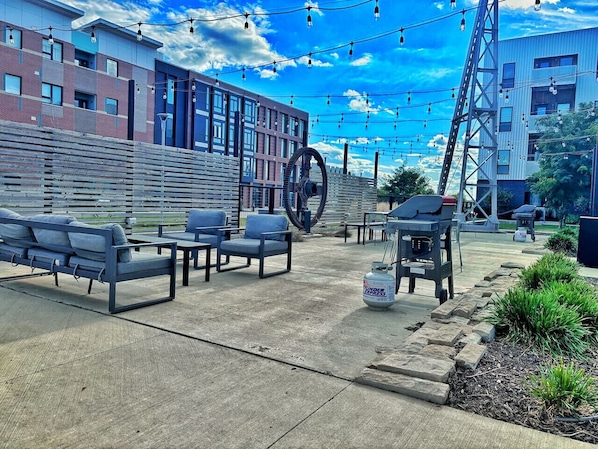 Un espace extérieur aménagé avec des bancs et des tables, une grande roue à eau et un coin barbecue.