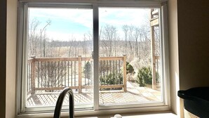 Ein Fenster mit Blick auf eine Holzterrasse und Bäume.