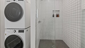 A laundry room with two stacked washing machines and a shower area with tiled walls and a showerhead. - Cozy / New 2-bedroom apartment in North Hollywood (Los Angeles)