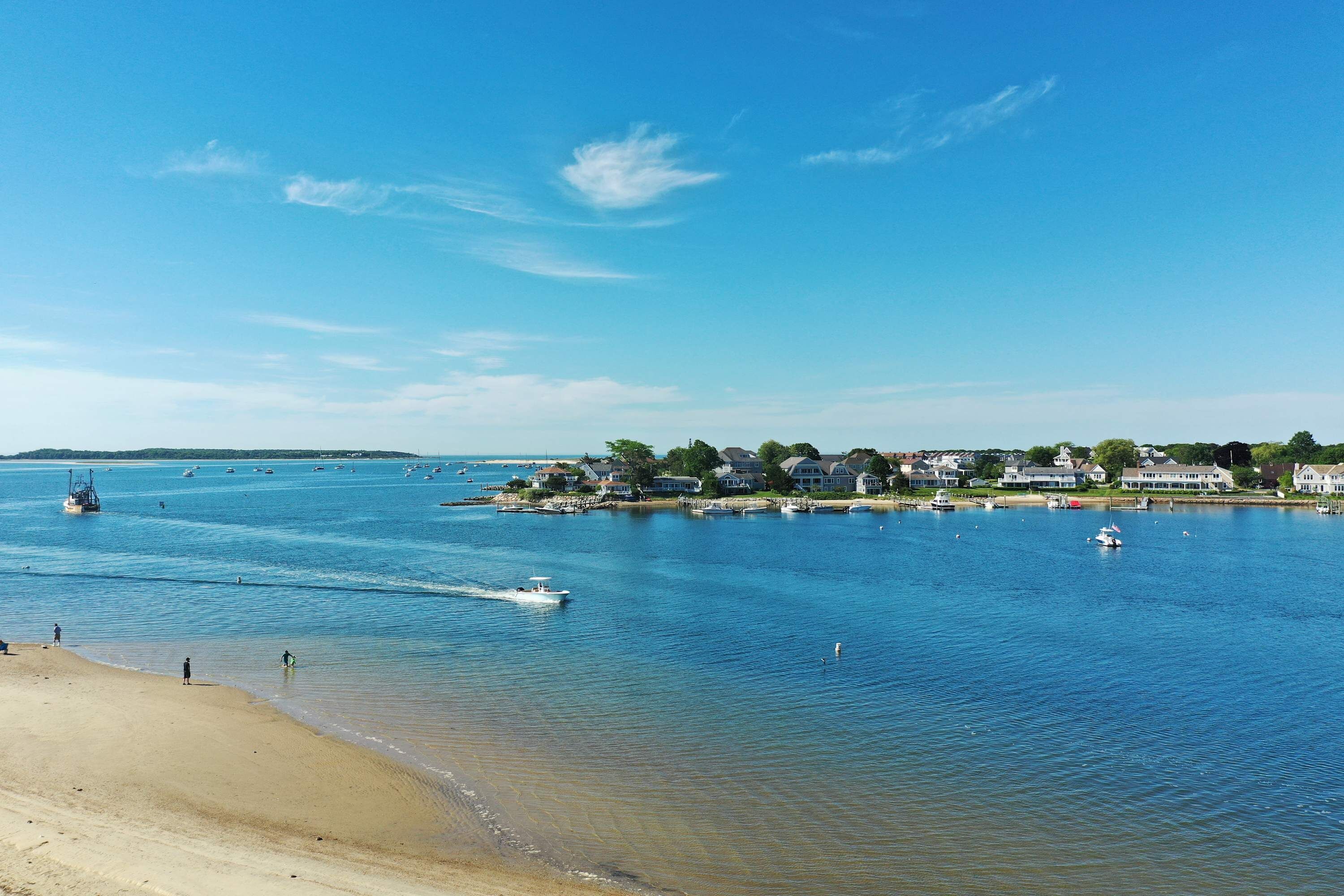 A coastal view with a beach, calm water, and houses along the shore.