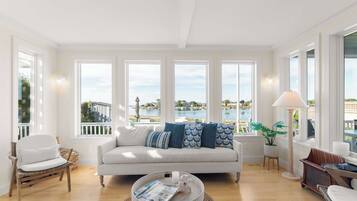 A spacious living room with a white sofa, a round coffee table, and a view of a body of water through large windows.