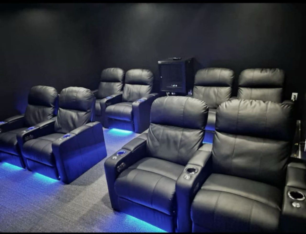 A row of black leather reclining chairs with built-in cup holders and a small screen in the center.