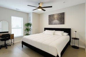Un dormitorio con cama, escritorio, silla, ventilador de techo y un cuadro en la pared.