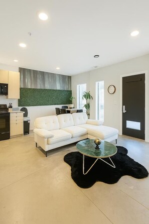 Un salon moderne avec un canapé blanc, une table basse en verre et un tapis noir à poils longs.