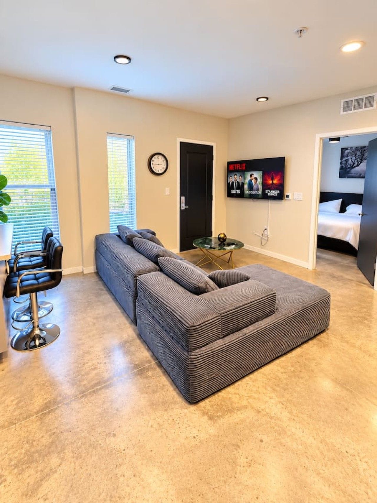 A modern living room with a sectional sofa, a TV mounted on the wall, and a dining area with a bar stool.
