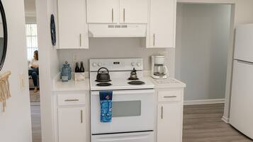 A compact kitchen with white cabinetry, a stove, a coffee maker, and a refrigerator.