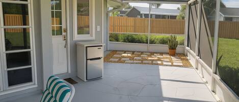 A covered patio area with a seating arrangement, a small refrigerator, and a potted plant.