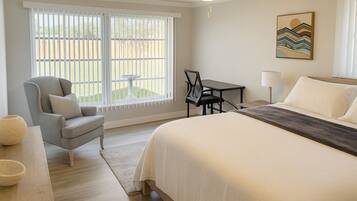 A bedroom with a large bed, a chair, a small table, and a window with a view of the outdoors.