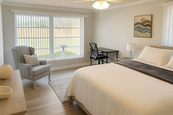A bedroom with a large bed, a chair, a small table, and a window with a view of the outdoors.