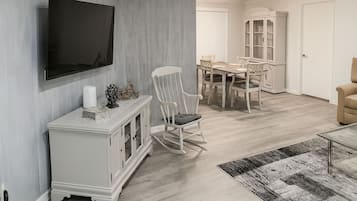 A dining area with a table and chairs, a television mounted on the wall, and a white cabinet with decorative items.