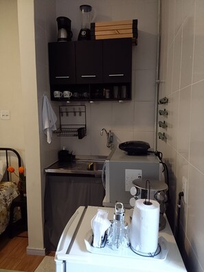 Cozinha compacta com forno embutido, máquina de café e chaleira no balcão.