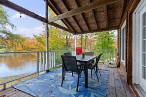 A covered outdoor area with a table and chairs, overlooking a body of water and autumn foliage.