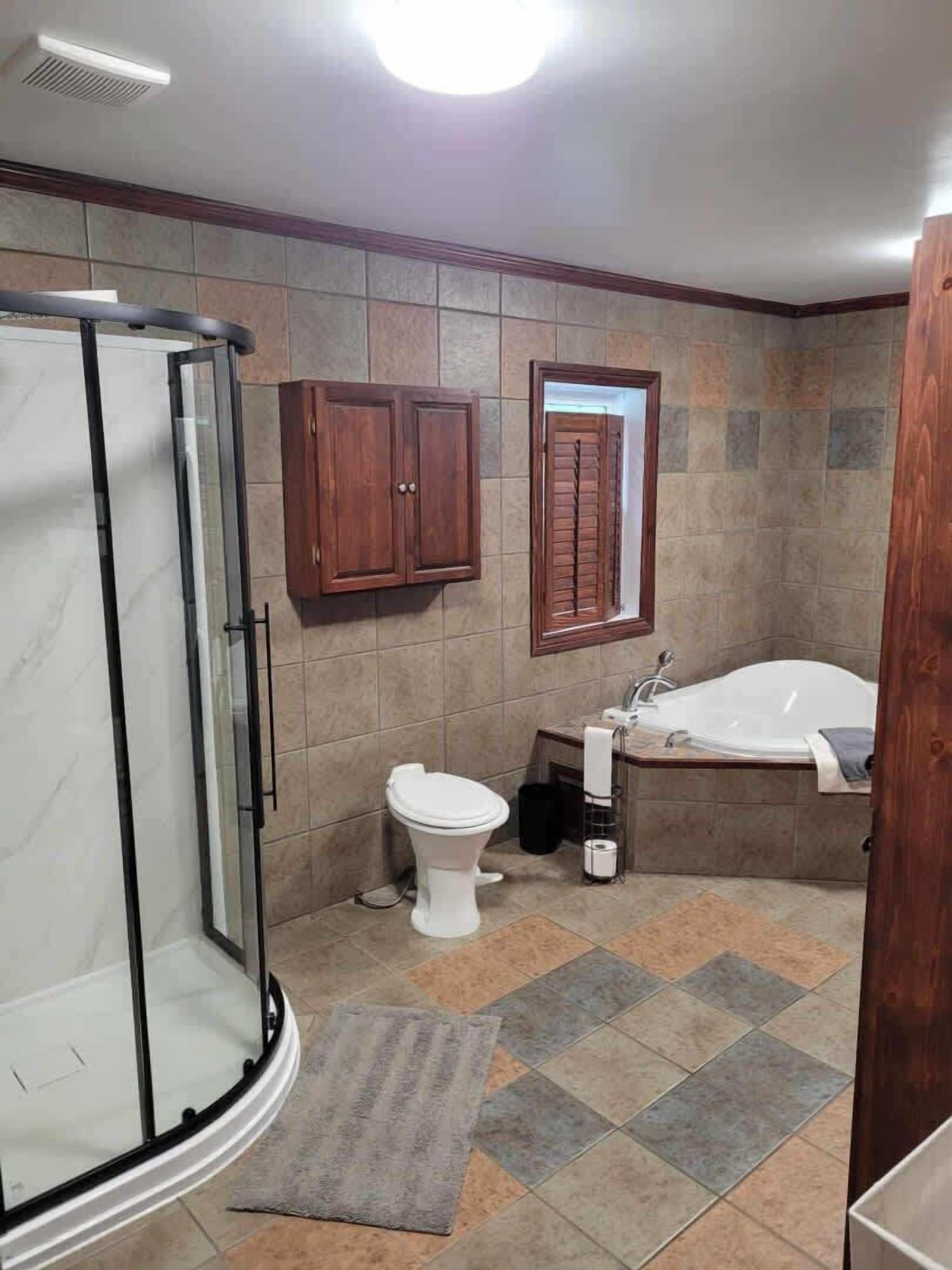 A bathroom with a glass shower enclosure, a toilet, a bathtub, and a wooden cabinet.