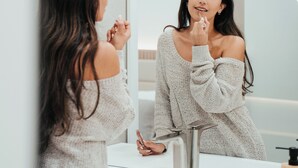 Une femme, vêtue d’une robe blanche à décolleté plongeant, se tient devant un miroir de salle de bain.