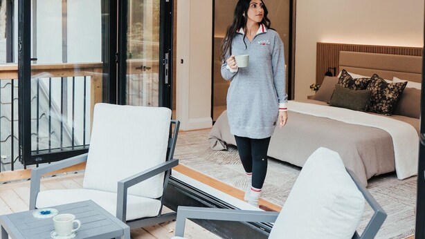 Une chambre moderne avec un grand lit, un canapé et un balcon aménagé avec des sièges d’extérieur.