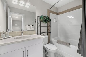 Un baño moderno con lavamanos, inodoro y ducha. Hay un espejo sobre el lavamanos y una repisa con plantas.