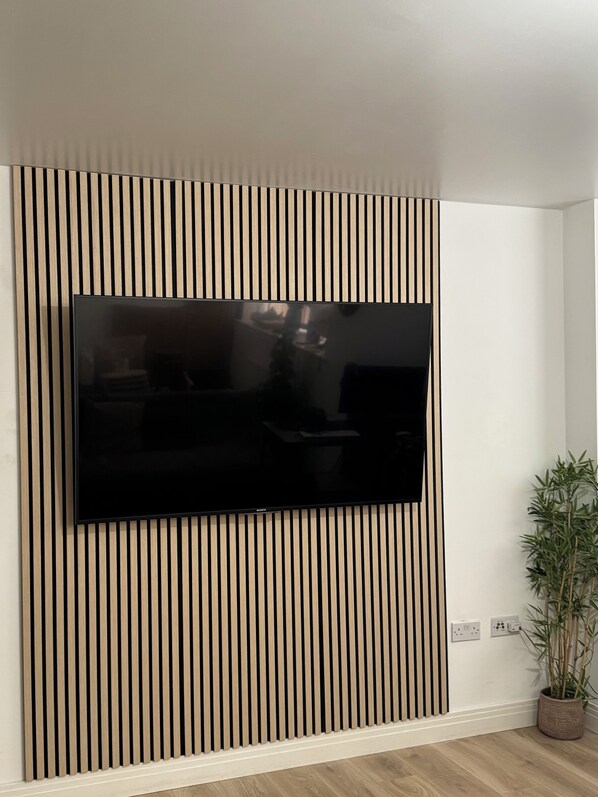 A flat-screen TV mounted on a wall with vertical wooden slats. - Modern Refurbished Apt in Stevenage Town Centre (Stevenage)